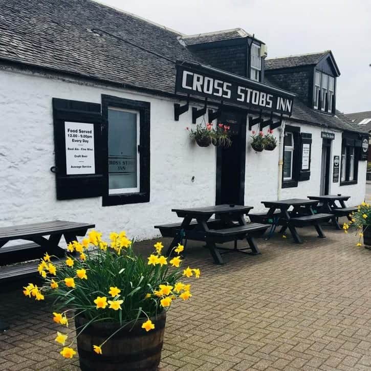 The whitewashed Cross Stobs Inn with its black sign and daffodils at the door