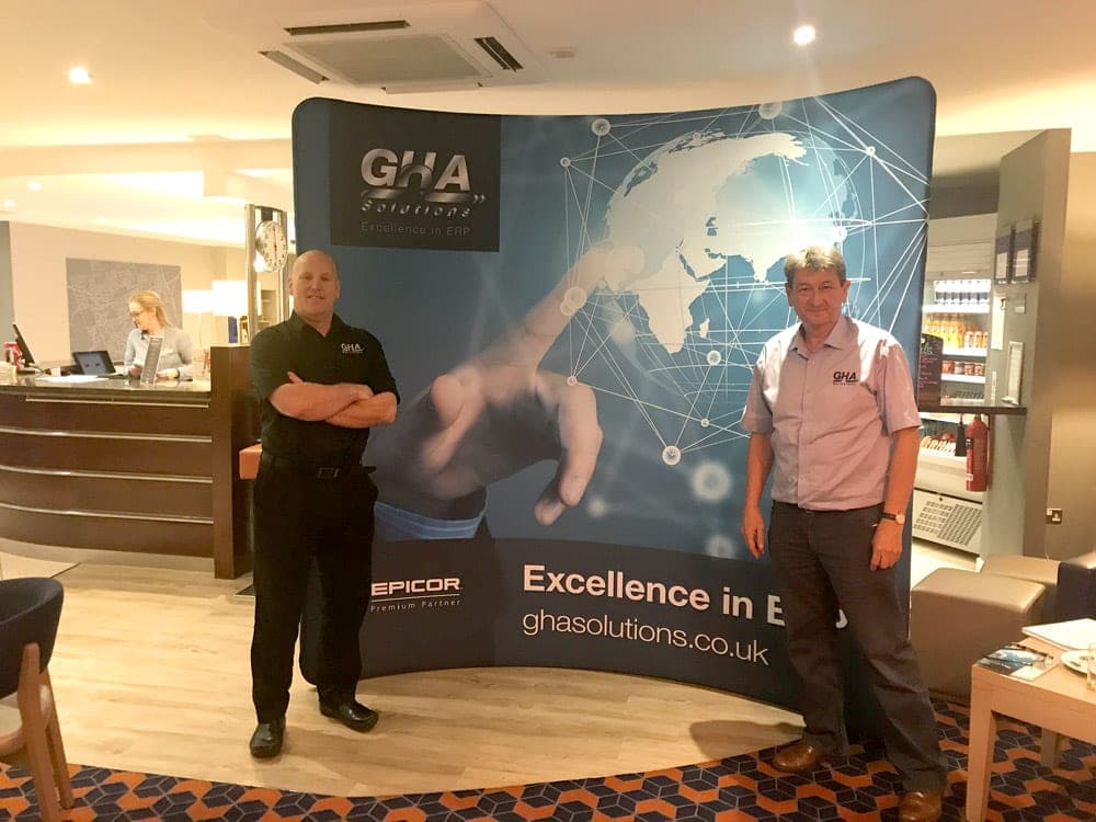 Two people on the GHA Solutions exhibition stand with a curved world-map backdrop